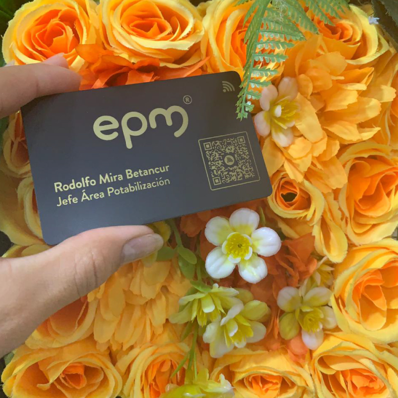 Dark business card held by a left hand over a bouquet of bright orange roses, featuring the epm logo, a QR code, and the name Rodolfo Mira Betancur with the title Jefe Área Potabilización.