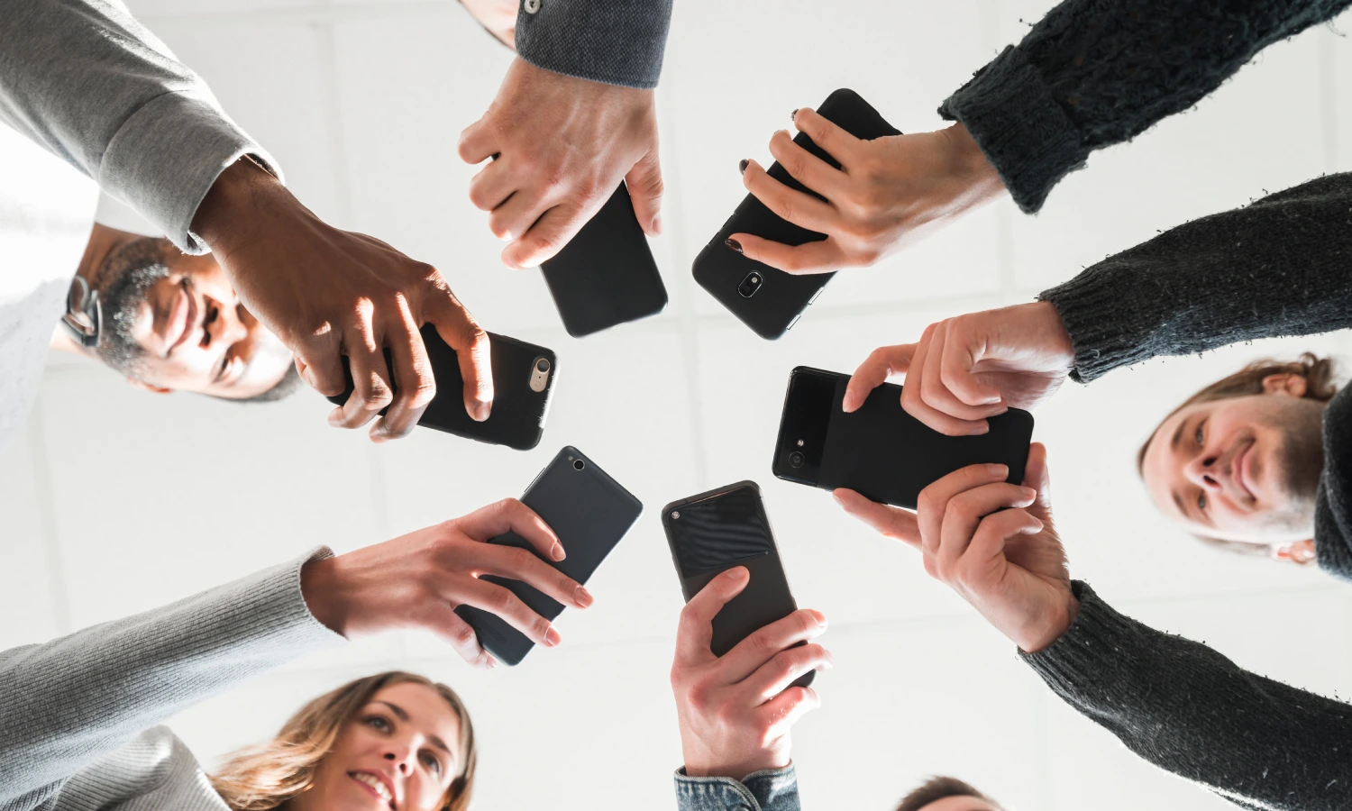 Group of people forming a circle, each holding a smartphone toward the center. An image of teamwork around mobile devices.