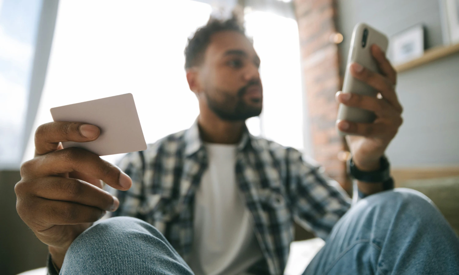 Man holding a credit card in one hand and a smartphone in the other, ready to shop online.