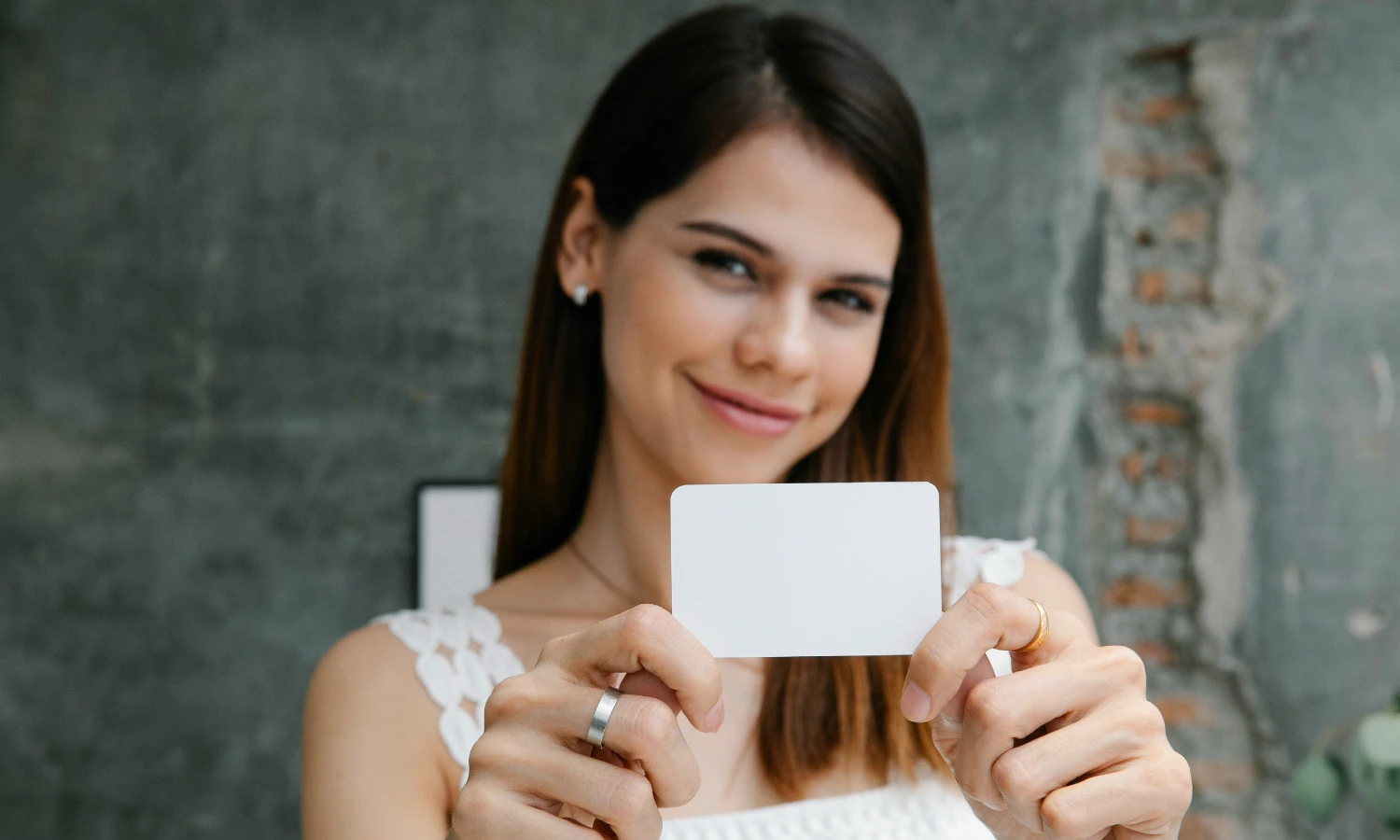 Smiling woman in a white top holds up a blank white card toward the camera.