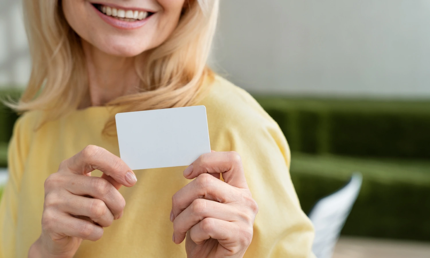 Smiling woman in a pale yellow top holds up a blank white card toward the camera.